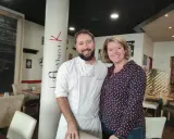 Le chef et sa collègue sourient devant la colonne "Authentik St Grégoire". L'ambiance chaleureuse du restaurant est palpable.