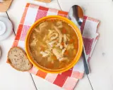 Aromaticzne flaki po zamojsku w pomarańczowej misce, obok kromka chleba i łyżka. Pyszne danie gotowe do spożycia.