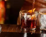 Ein Drink wird in ein Glas mit Eis und Orangenzeste gegossen. So trinkt man Whisky.