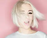 Mujer con cabello rubio platino y corte recto al hombro, con un ojo visible y labios rosados abiertos.