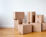 Stapel von braunen Kartons auf einem Holzboden, bereit für den Umzug oder zur Aufbewahrung.