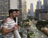 Two men embrace on a balcony overlooking a city street, a scene reminiscent of some of the most gay cities in the US.