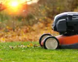 Lawn mower ready for fall lawn maintenance. Fallen leaves litter the green grass as the sun sets.