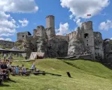 Ruiny zamku na skale, część wyżyny krakowsko-częstochowskiej, z widownią siedzącą na trawie.