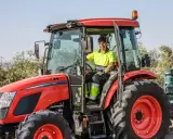 Un homme souriant conduit un tracteur rouge, une machine pour arracher des bambous, prêt à travailler dans un champ.