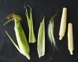Corn husks, silk, and cobs are arranged on a dark surface. This visual might inspire thoughts on how far apart to plant corn for optimal growth.