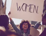 Frauen demonstrieren für Gleichberechtigung. Eine Frau hält ein Schild mit der Aufschrift "WOMEN". Das zeigt, was feminist ist: eine Stimme für Frauen.