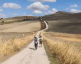 Due pellegrini camminano su una strada sterrata in un paesaggio collinare, forse da dove parte la Via Francigena.