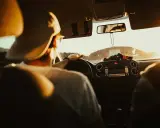 Hombre con gorra al volante, listo para planificar viaje en coche. El sol ilumina el interior del vehículo.