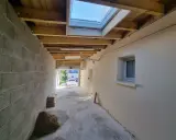 Vue d'une extension en cours de construction avec reprise de toiture, poutres apparentes et un puits de lumière.