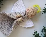 Un tierno angel amigurumi de ganchillo, con alas blancas y un cuerpo gris, adornado con ramitas verdes.