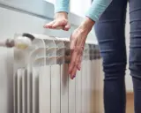 Dłonie sprawdzają temperaturę grzejnika, zastanawiając się, dlaczego grzejnik jest zimny na dole.