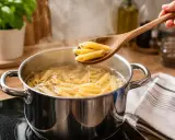 Drewniana łyżka z penne nad garnkiem wrzącej wody. Prosty sposób, jak ugotować makaron do perfekcji.