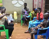 Kvinnor och barn samlas för vaccination i Uganda. En kvinna i väst visar upp papper.