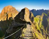 Pfad über Felsen zum Pico Ruivo, Madeira. Steile Hänge, grüne Vegetation und ein schmaler Weg mit Seilsicherung.