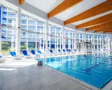 Wnętrze z basenami hotelowymi, leżakami i dużymi oknami z widokiem na budynek hotelowy.