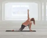 Kvinna utför en vriden yogaställning i ett ljust, öppet rum. Hon fokuserar på sin power yoga-träning.