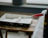 Wanna malarska z białą farbą i wałkiem czeka na rozpoczęcie malowania ścian od okna.