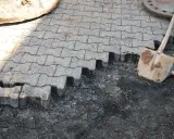 Fragment nawierzchni z kostki brukowej w trakcie układania, obok łopata.