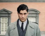 Uomo con trench, camicia a righe e cravatta, con un'espressione seria. Un ritratto creato per mano mia.