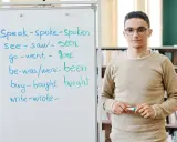 Nauczyciel wyjaśnia formy czasowników, od prostych do tych w **far stopień wyższy i najwyższy**.