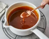 Flüssiges Karamell tropft von einem Löffel in einen Topf. Das Zucker karamellisieren ist fast perfekt.