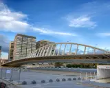 El moderno puente de la Exposición cruza un río, con edificios altos al fondo bajo un cielo azul con nubes.