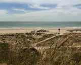 Strand von Conil de la Frontera mit Dünen, einem Strandcafé und Sonnenschirmen. Das Meer ist ruhig, der Himmel ist bewölkt.