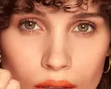 Primer plano de una mujer con rizos oscuros y maquillaje color coral vibrante en los labios.