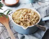 En skål med krämiga stuvade makaroner, toppad med svartpeppar. En träsked ligger bredvid.