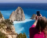 Widok na turkusowe morze i skaliste wysepki, w tym Cameo Island. Kobieta robi zdjęcie telefonem.