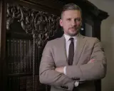 Mężczyzna w garniturze stoi przed regałem z książkami.