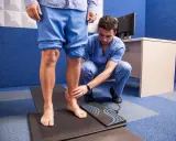 Un podologue examine le pied d'un patient sur un tapis de mesure, dans le cadre d'une consultation de pédicurie.