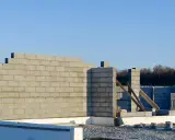 Budowa domu w toku. Wznoszona jest ściana nośna z bloczków betonowych, widoczne fundamenty i materiały budowlane.