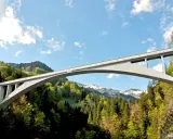 El puente de Salginatobel se alza majestuoso sobre un valle verde, con picos nevados al fondo.