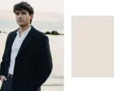 Davide Avolio, con le mani in tasca, indossa un cappotto scuro e una polo bianca, con il mare sullo sfondo.