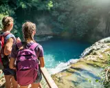 Due escursioniste con zaini ammirano una cascata turchese durante il loro trekking in Toscana.