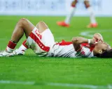 Fußballer liegt erschöpft auf dem Rasen, die Hände im Gesicht. Nach einem harten Spiel braucht er Regeneration.