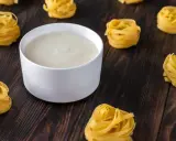 Un bol de béchamel sans beurre crémeuse, entouré de nids de pâtes fraîches sur fond de bois sombre.