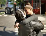 Para mi recenzje The Sims 4, ta scena oddaje emocje, które można przeżyć w grze. Para przytula się na ulicy, w tle widać samochody i budynki.