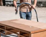 Un homme utilise un appareil pour le décapage bois sur un bureau. La surface est partiellement nettoyée, révélant le bois brut.
