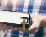 Osoba w kratę trzyma Biblię z drewnianym krzyżem, symbolizującym dwa przykazania miłości.