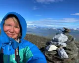 Kvinna på berg i Sverige med en stenröse i förgrunden och snöklädda berg i bakgrunden.