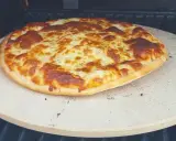 Upieczona pizza z roztopionym serem na kamieniu do pizzy na grillu.