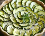 Un délicieux tian de courgettes, joliment disposé en spirale, parsemé d'herbes et de fromage râpé, avec une touche de basilic frais au centre.