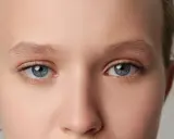 Zbliżenie na oczy młodej osoby. Widoczne niebiesko-zielone tęczówki, rzęsy i brwi. Skóra gładka, bez widocznych oznak dystrofii Fuchsa.
