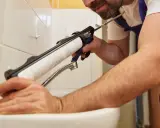 Un homme applique une bonde silicone autour d'un lavabo avec un pistolet.
