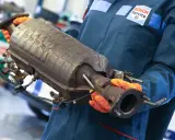 Mechanik w rękawiczkach trzyma zużyty katalizator, prawdopodobnie z Peugeota p2448.