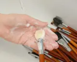 Mano con espuma jabonosa limpiando brochas de maquillaje en un lavabo.