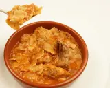 Un plato humeante de comida típica de Albacete, con trozos de carne y pasta en una salsa rojiza.